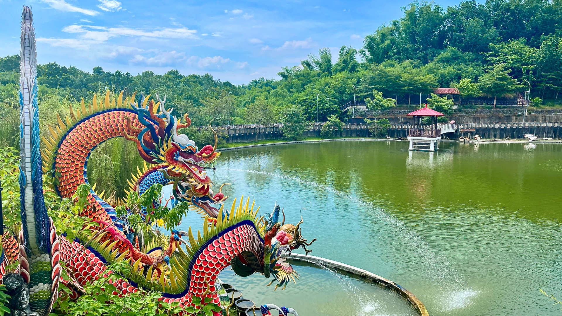 Statues of four colorful dragons beside a lake, with water spraying out of their mouths.