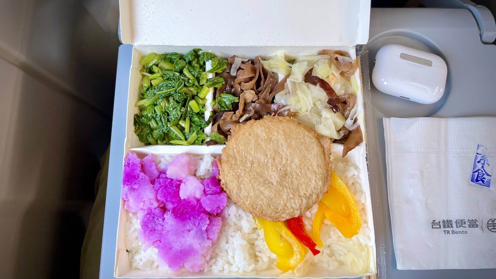 An open bento box containing white rice, a round tofu patty, and six types of vegetable.