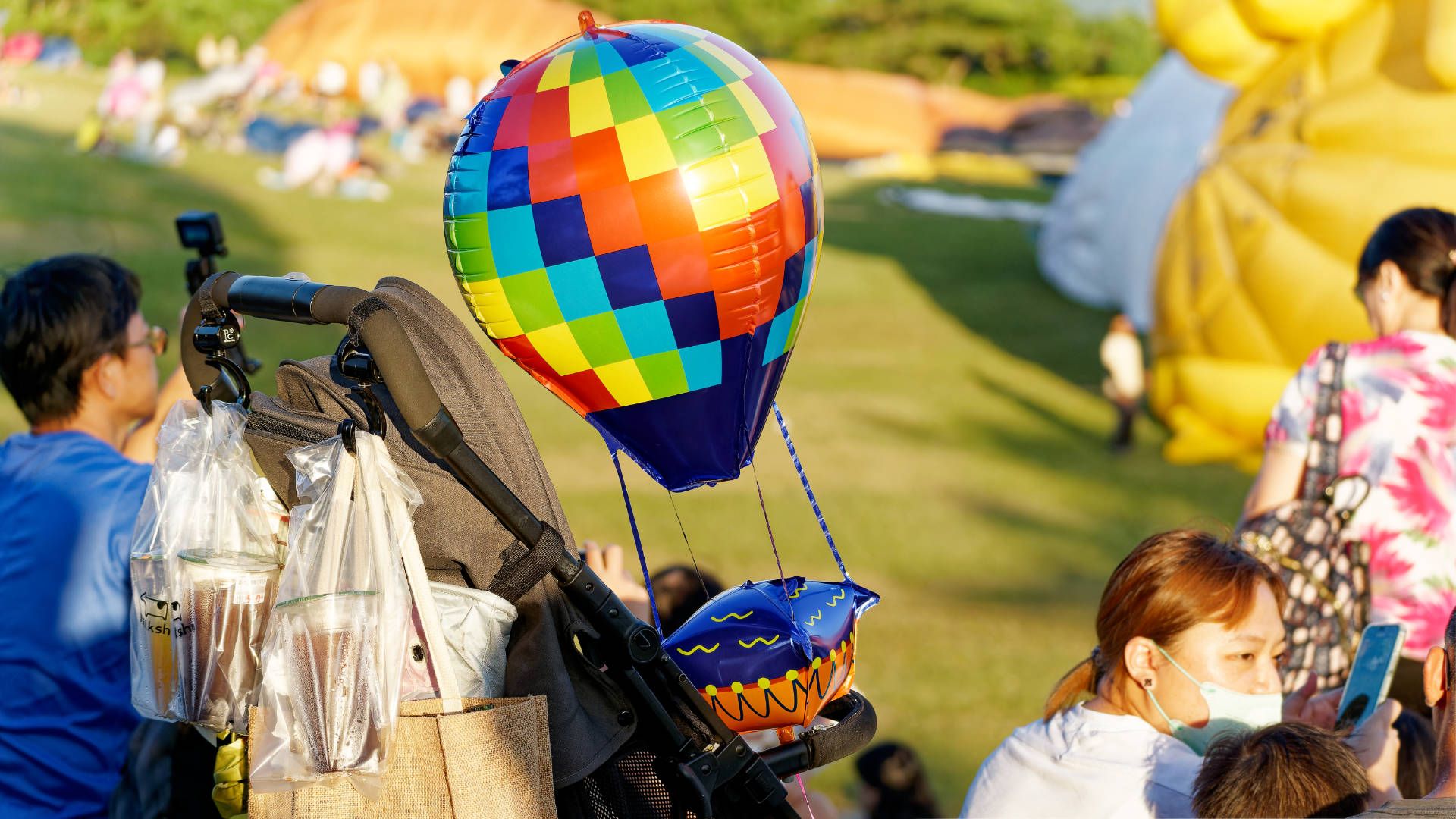 An inflated toy balloon attached to a baby stroller in the crowd.