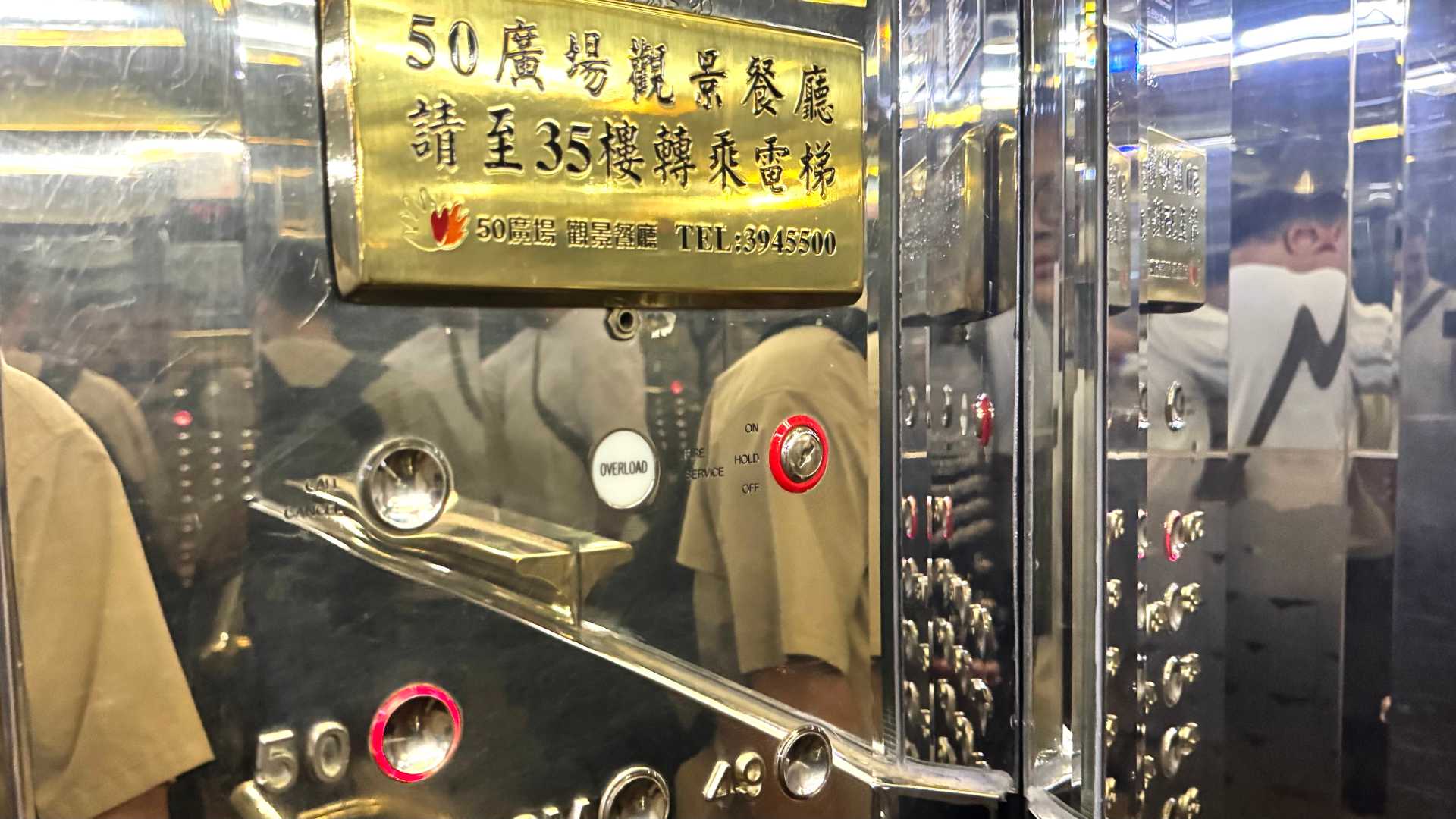 Elevator interior. An old-style golden plaque contains characters in Chinese. The button for the 50th floor is illuminated.