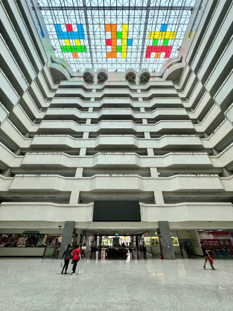 Atrium of the Kaohsiung City Government Building. The wide-angle shot shows both the reflective marble foor, with a few people walking on it, and the stained glass ceiling 11 floors up. Integrated into the ceiling are six stylized Chinese characters.