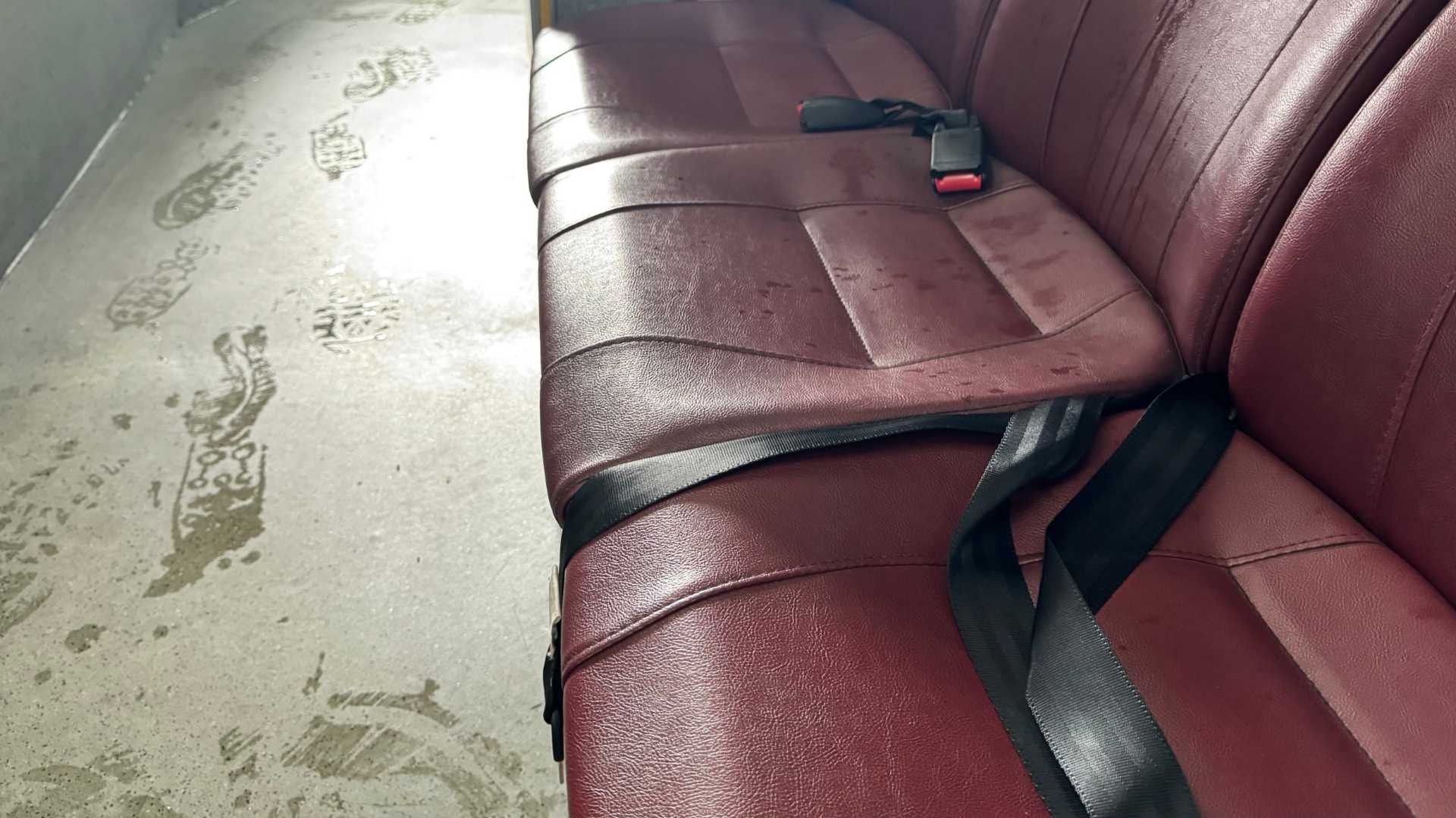 Seatbelts on the seats of a commuter bus, with wet footprints on the foor next to the seats.