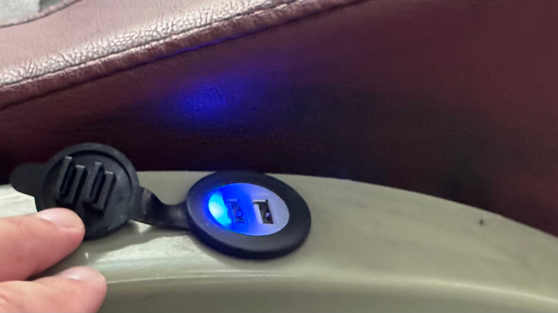 A watertight lid being held open to reveal two USB ports underneath, integrated into the side of a bus seat.