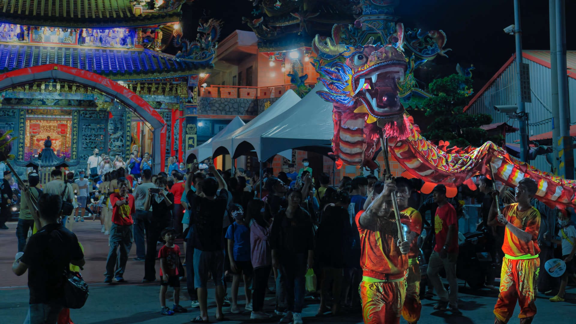 A Chinese Dragon dance performance in front of a crowded temple at night.