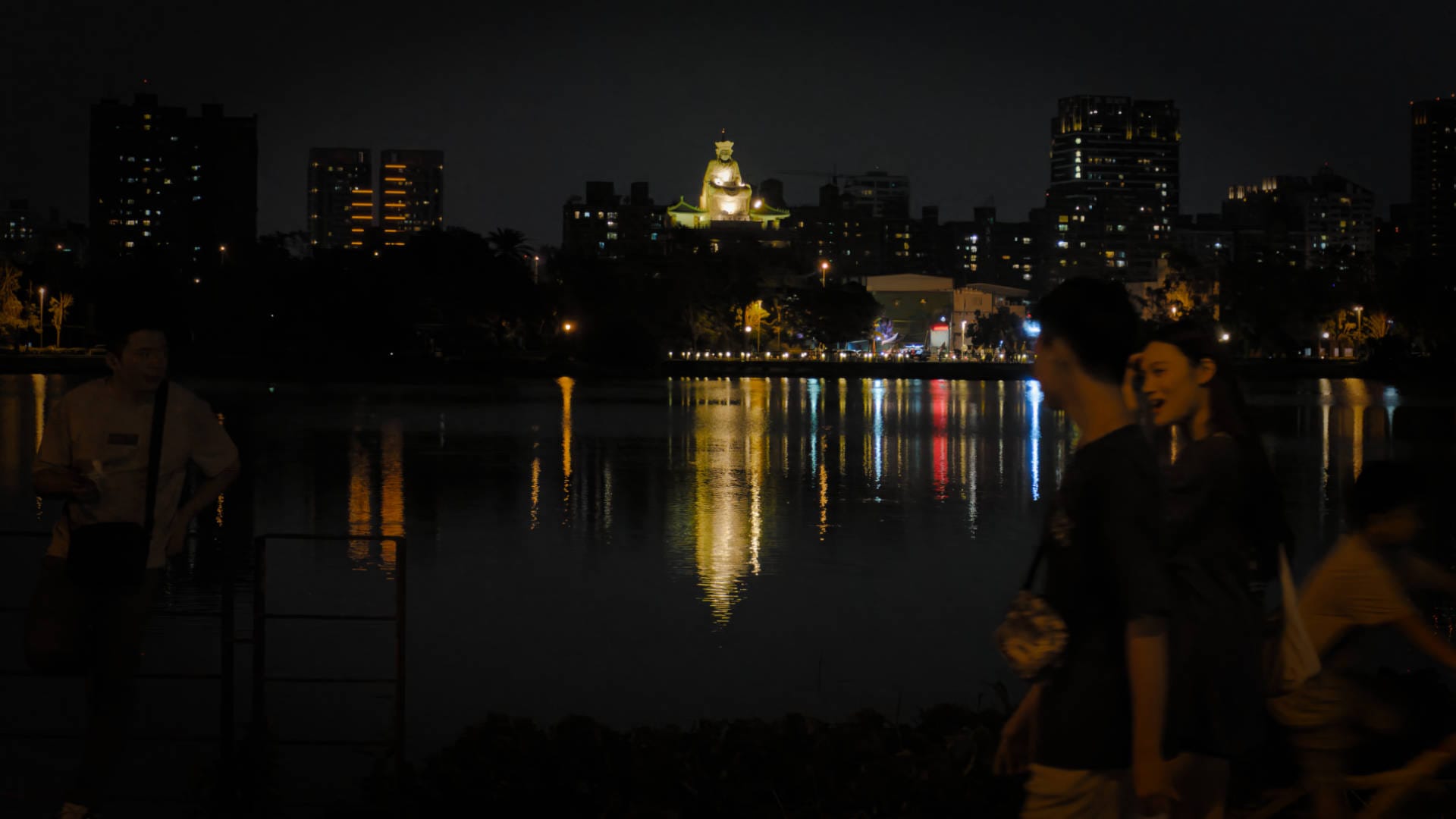 View of large statue of Guanyin, illuminated at night and reflected in the still water of Lotus Pond.