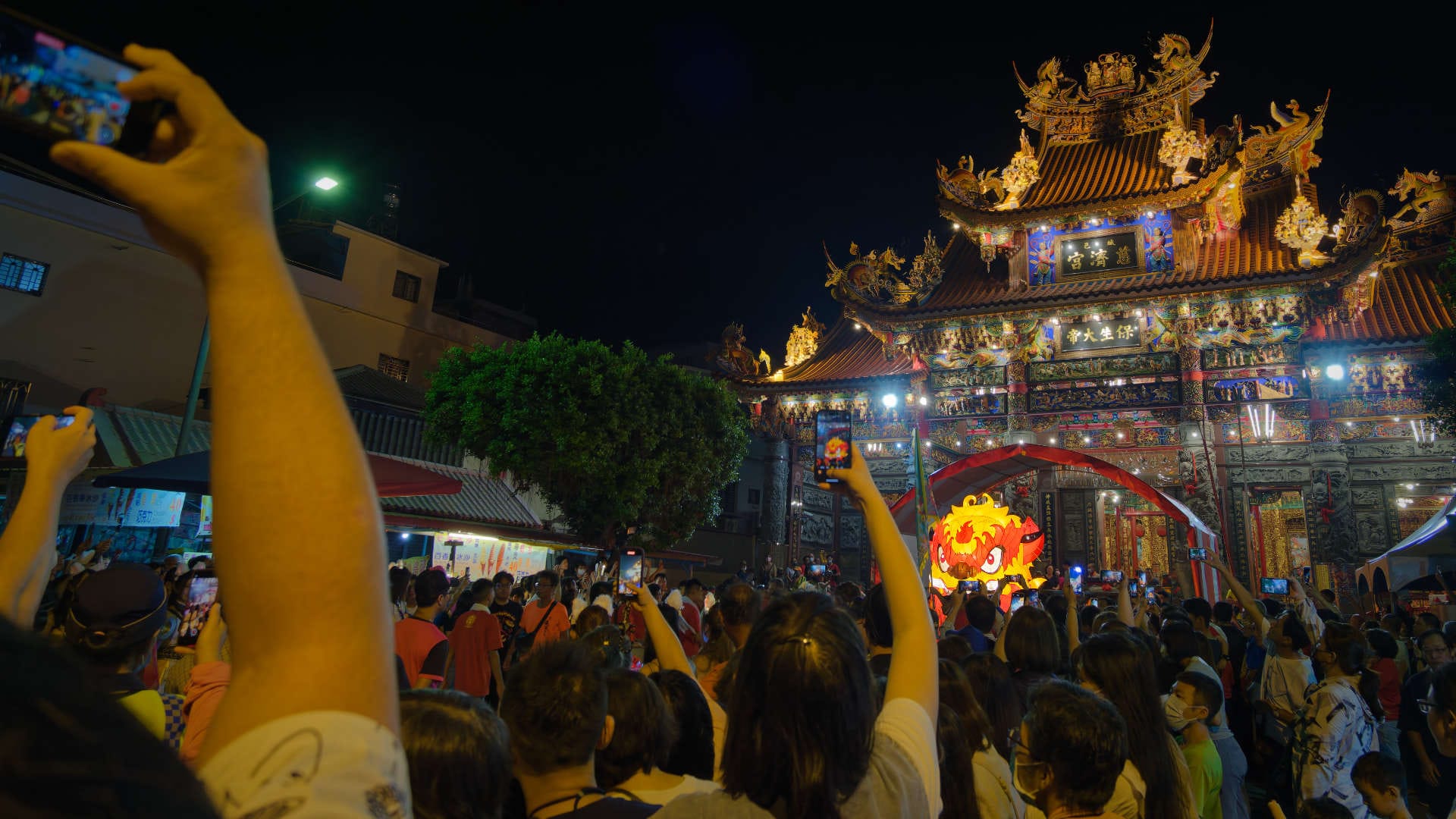 People holding cellphones high above their heads, taking photos of a Fire Lion above the crowd at the Kaohsiung Zuoying Wen Nian Festival.