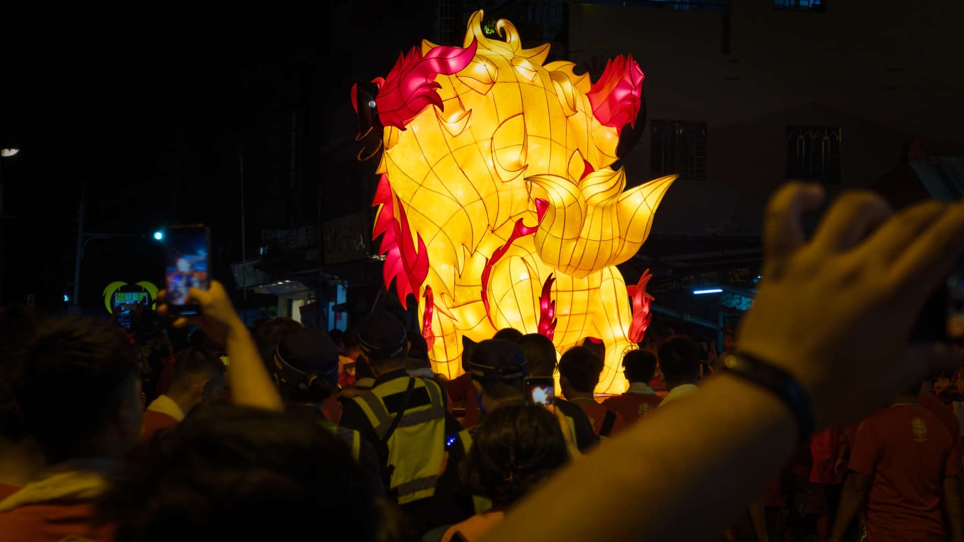 Rear view of a large Fire Lion lantern as it is carried away through a dense crowd.