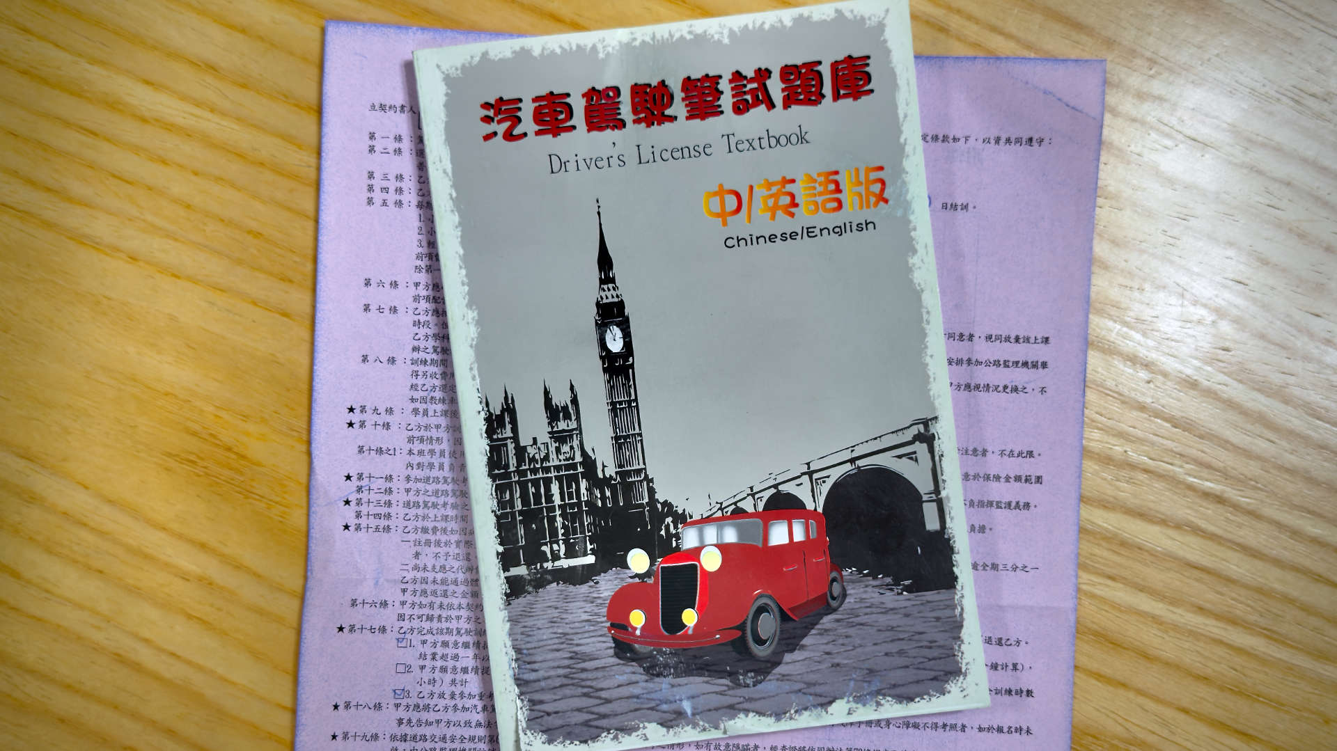 A book titled Driver’s License Textbook Chinese/English, resting on a pile of Chinese-language paperwork.