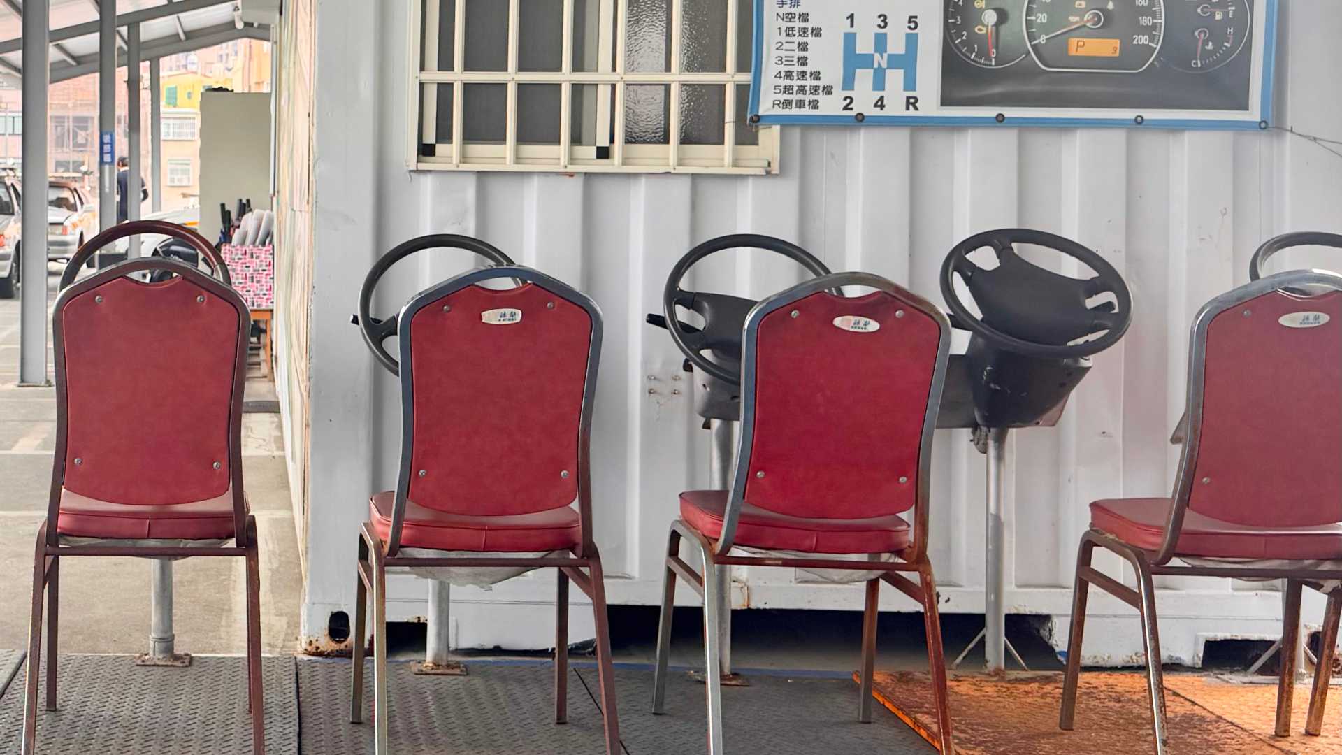 A row of car steering wheels mounted on an outdoor platform, effectively a rudimentary driving simulator.