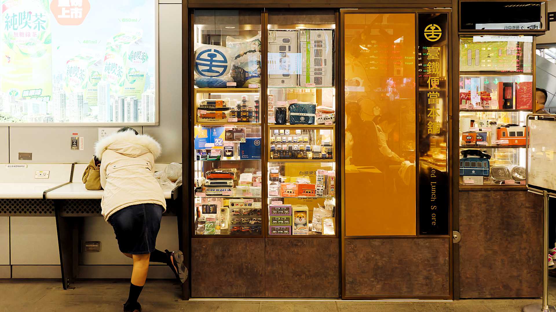 A traveler leaners over their charging phone outside a gift shop at Kaohsiung Station.