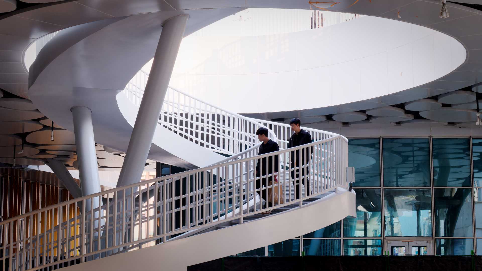 Two people walking down a spiral staircase at Kaohsiung Station.