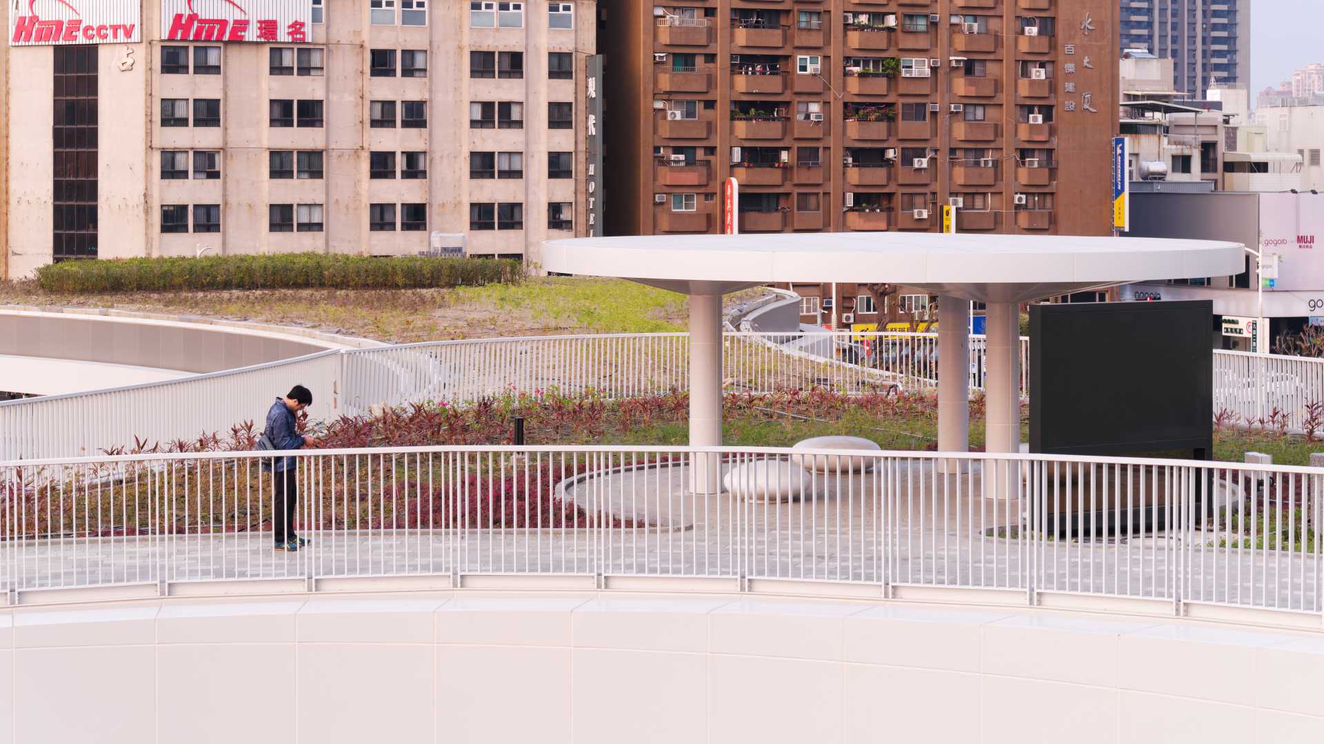 A man checks his phone, standing on the rooftop garden of Kaohsiung Station.