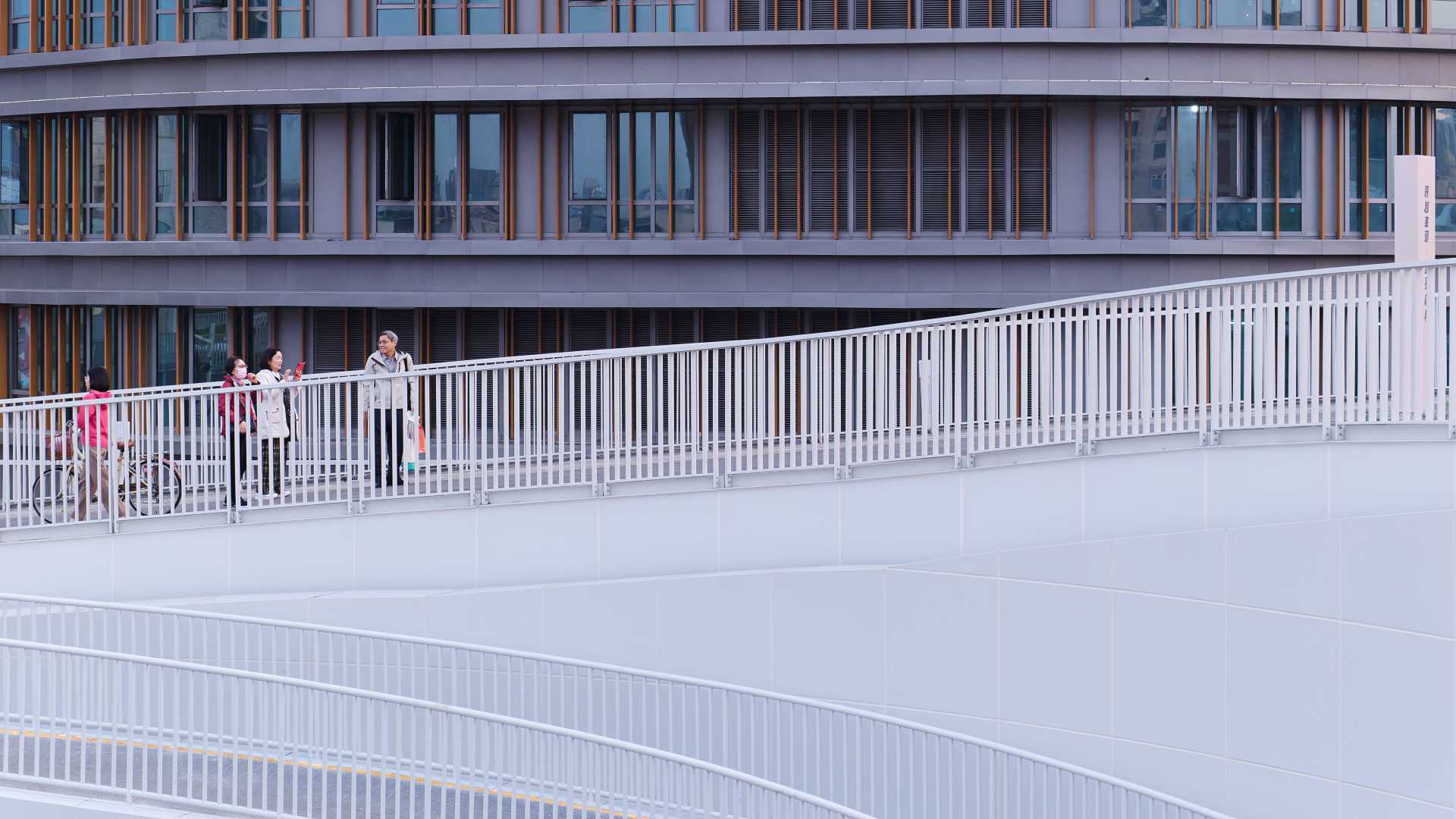 Three people climb a long spiral ramp, outdoors at Kaohsiung Station.