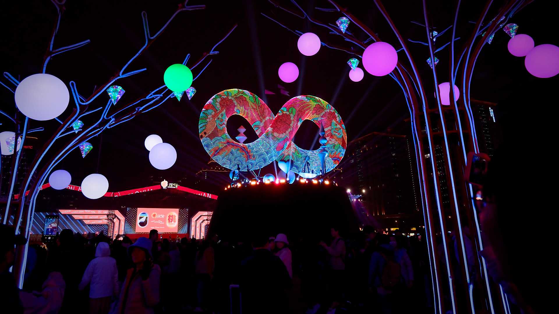 Viewed through neon trees, the main lantern of the festival looks like a 3D infinity symbol. It is on a rotating stage, and covered in animated patterns of cobra, mountains, and sea.