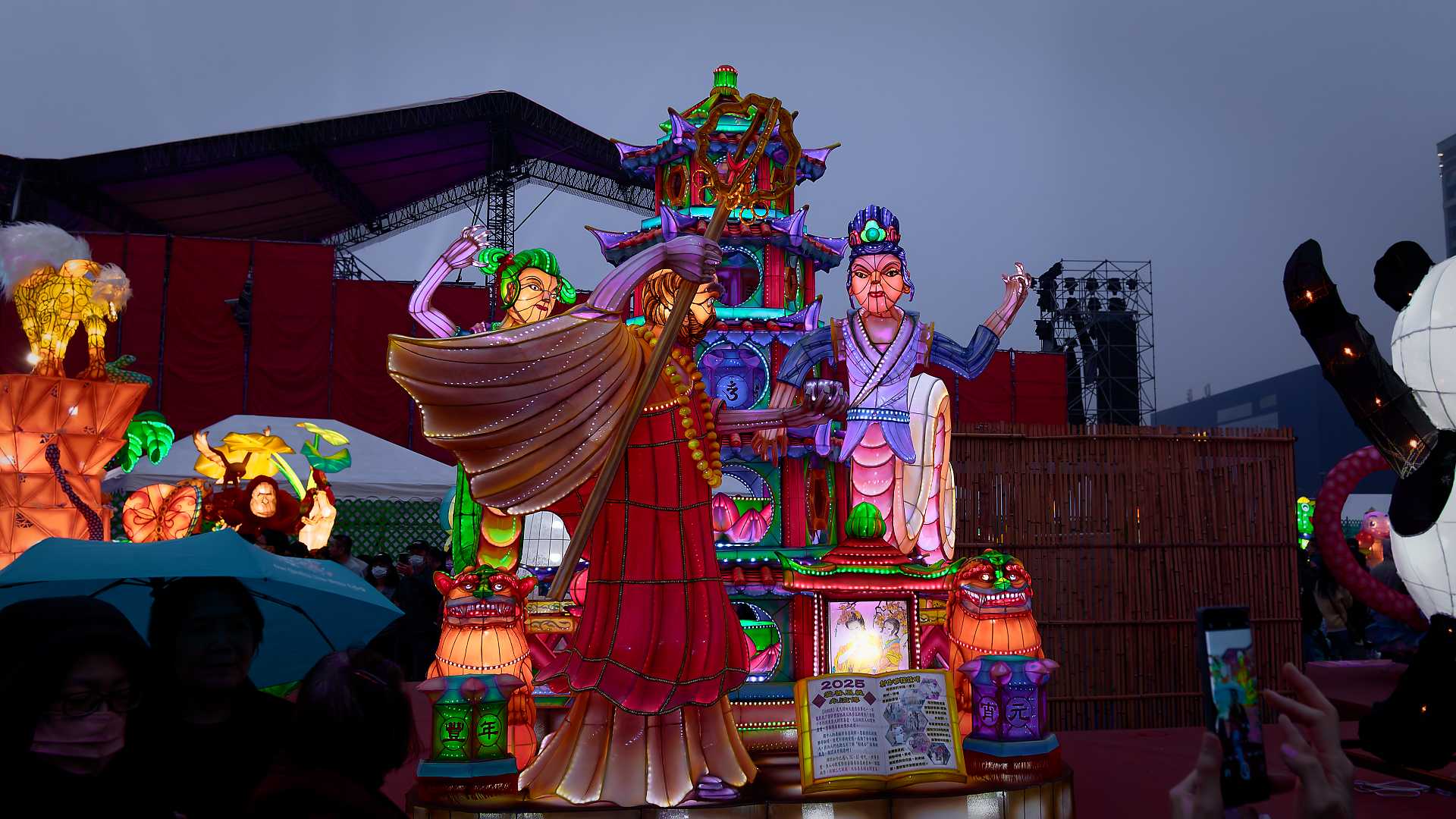 Lantern in the shape of three exquisitely-dressed people standing around a pagoda.