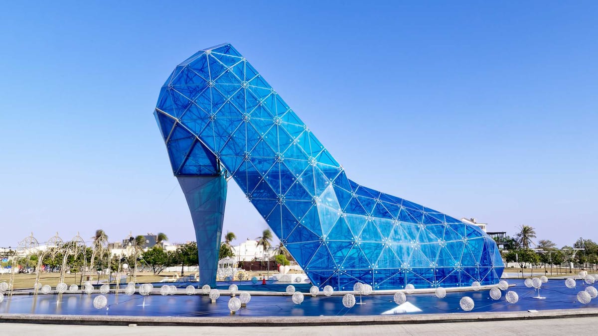 Long exposure of a glass building in the shape of a high-heel shoe, surrounded by a shallow pond.