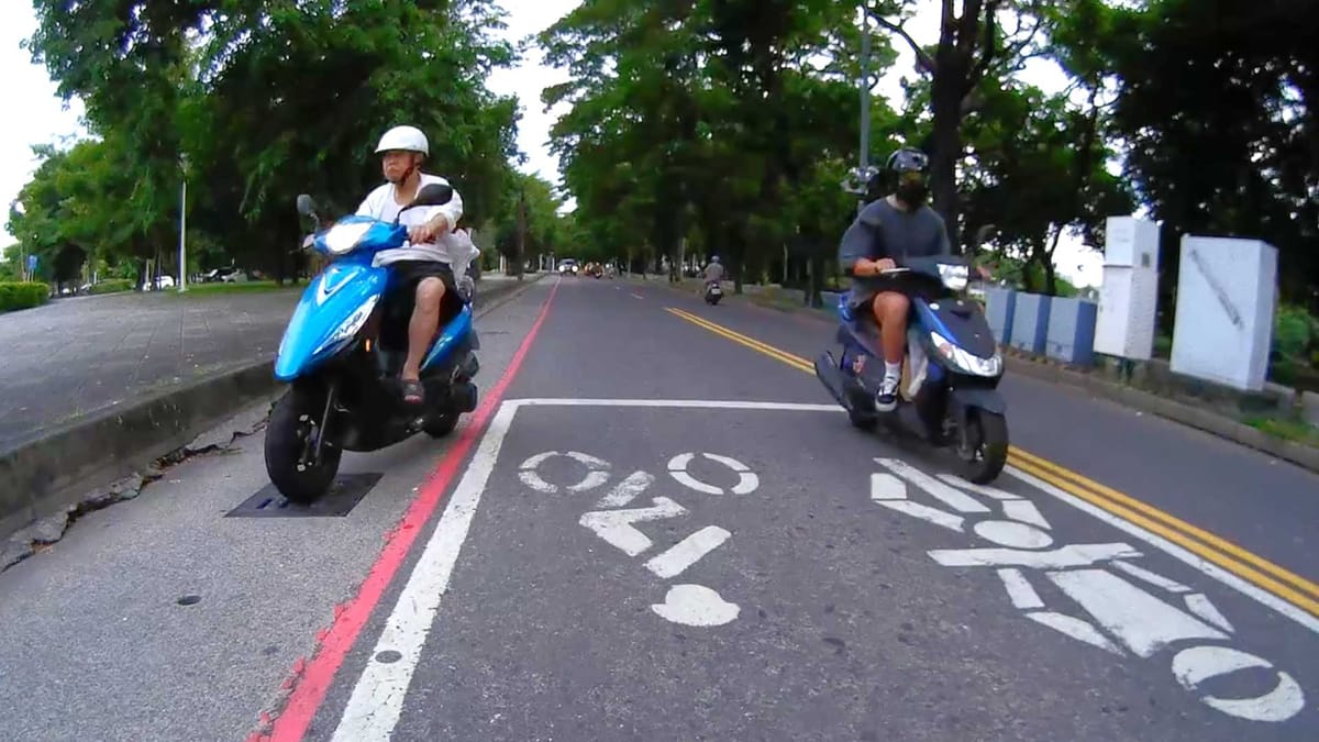 Screenshot of motorcycle dashcam footage showing an elderly man driving his scooter in a roadside gutter.